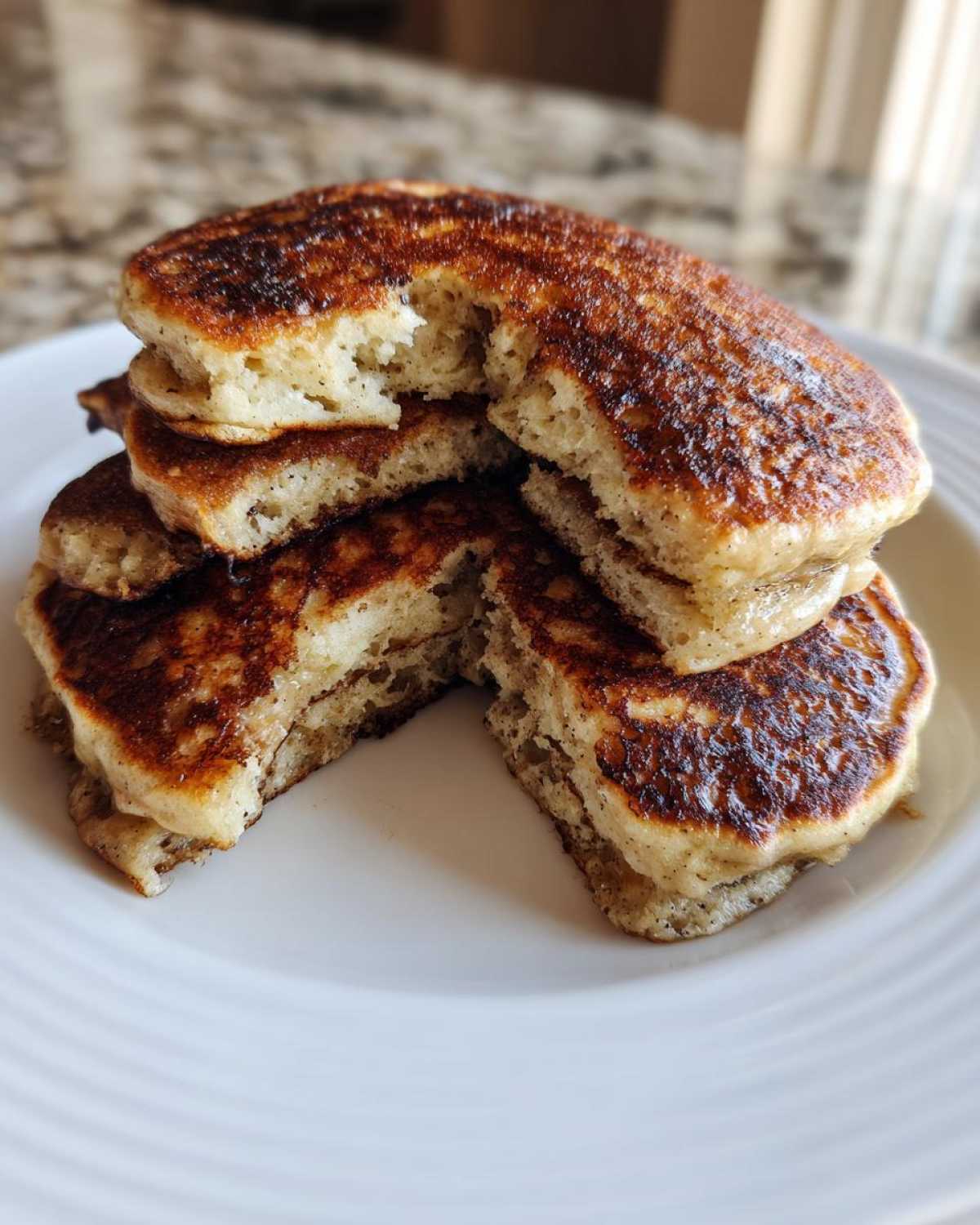 A stack of golden-brown Vegan Banana Oat Pancakes, with a piece taken out to show the fluffy interior texture.