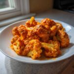 Brightly colored florets of Vegan Cauliflower Tikka Masala coated in a rich, orange sauce on a white plate.