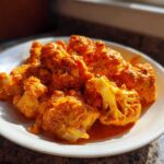 Close-up of bright orange, saucy cauliflower florets from the Vegan Cauliflower Tikka Masala recipe served on a white plate.