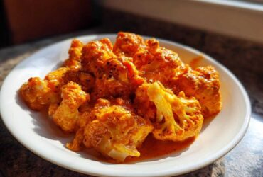 Close-up of bright orange, saucy cauliflower florets from the Vegan Cauliflower Tikka Masala recipe served on a white plate.