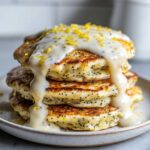 A tall stack of fluffy Vegan Lemon Poppy Seed Pancakes drizzled with thick glaze and lemon zest.