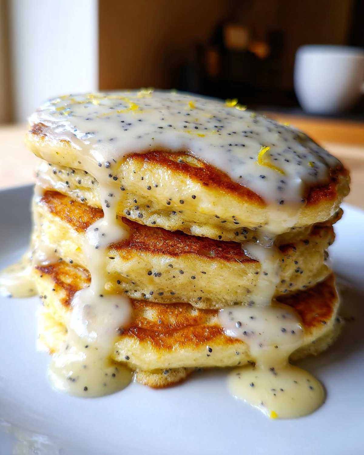Close-up of a stack of fluffy Vegan Lemon Poppy Seed Pancakes drizzled with lemon glaze.