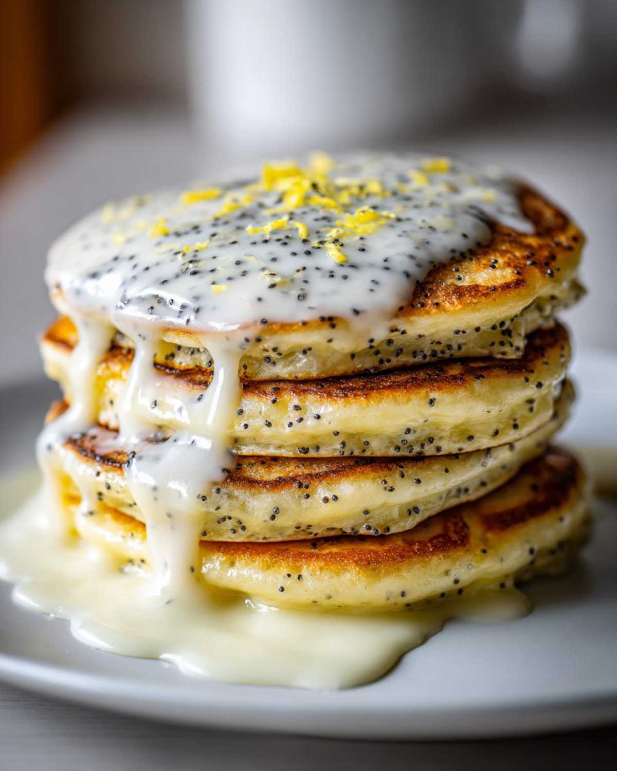 Close-up of a stack of fluffy Vegan Lemon Poppy Seed Pancakes drizzled with a thick lemon glaze and topped with zest.