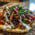 Close-up of Vegan Mushroom Shawarma served open-faced on pita bread with white sauce, tomatoes, and red onion.