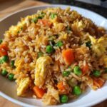 A close-up of delicious Vegetable Fried Rice with Sesame Ginger Sauce, featuring rice, peas, carrots, and scrambled egg pieces.