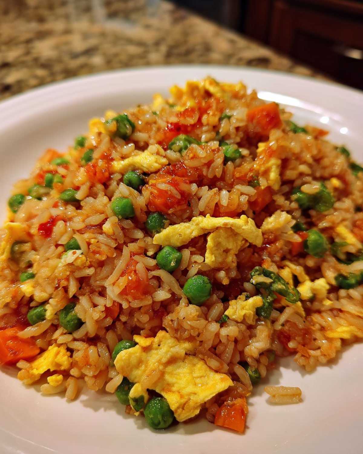 Close-up of a generous serving of Vegetable Fried Rice with Sesame Ginger Sauce, featuring rice, peas, carrots, and scrambled egg.