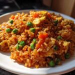 A close-up, sunlit serving of Vegetable Fried Rice with Sesame Ginger Sauce, featuring rice, peas, carrots, and scrambled egg.