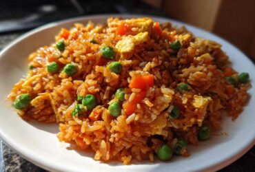 A close-up, sunlit serving of Vegetable Fried Rice with Sesame Ginger Sauce, featuring rice, peas, carrots, and scrambled egg.