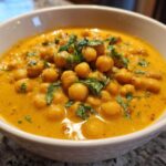A close-up of a white bowl filled with rich, yellow Vegetarian Chickpea Curry with Coconut Milk, topped with fresh cilantro.