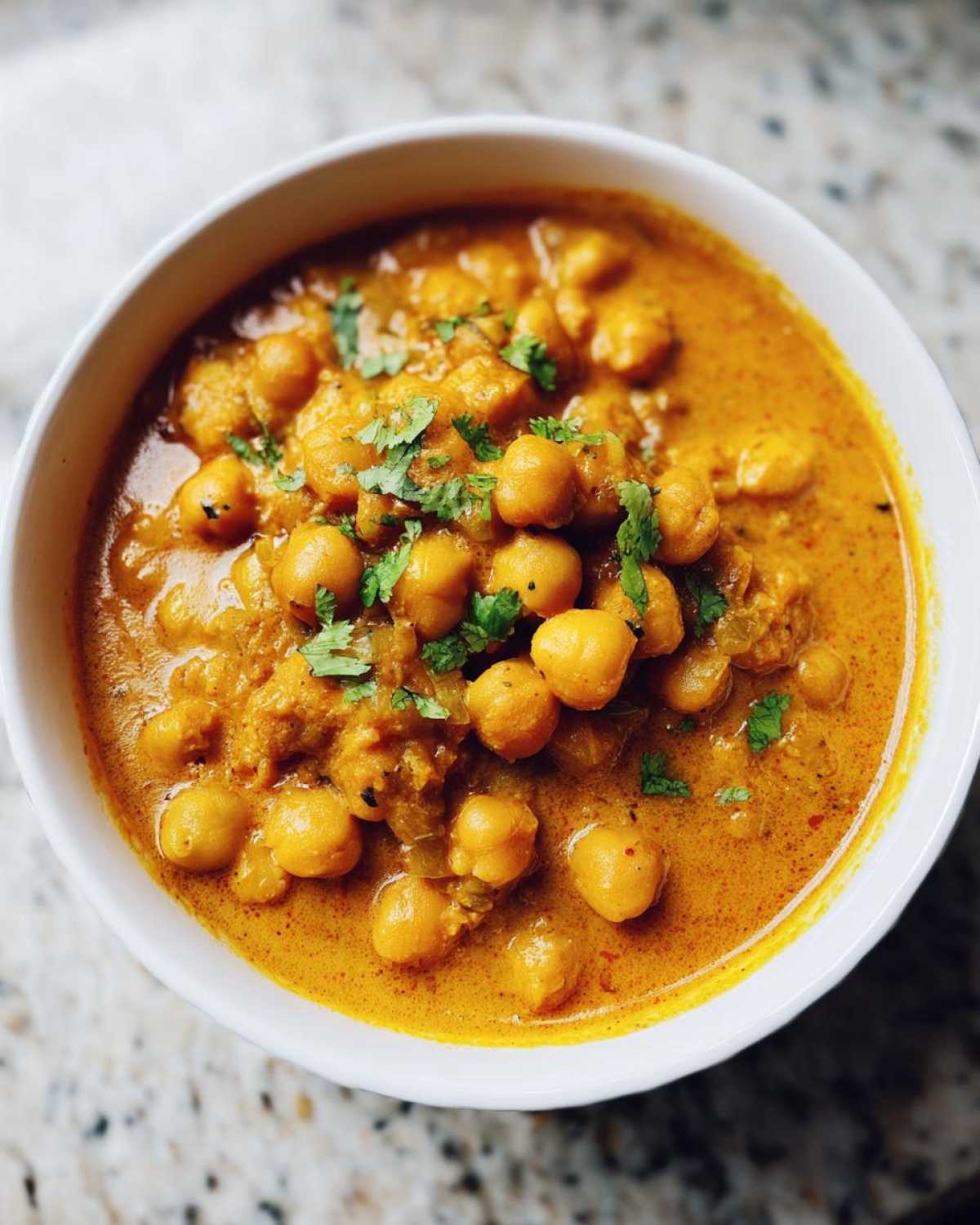 Close-up of a white bowl filled with rich, orange Vegetarian Chickpea Curry with Coconut Milk, garnished with fresh cilantro.