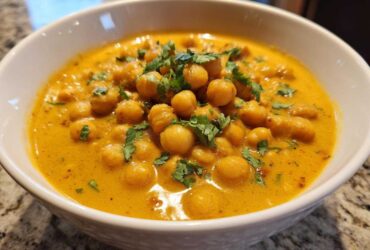 A close-up of a white bowl filled with rich, yellow Vegetarian Chickpea Curry with Coconut Milk, topped with fresh cilantro.