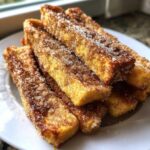 A stack of golden brown Air Fryer French Toast Sticks generously coated in cinnamon sugar on a white plate.