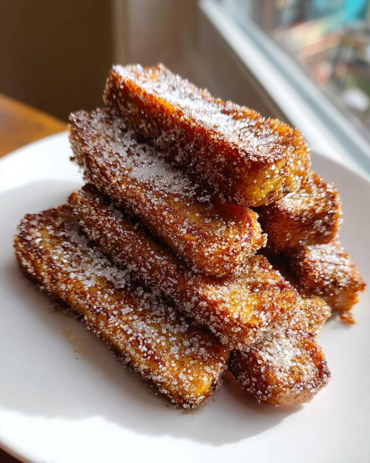 A stack of golden brown Air Fryer French Toast Sticks generously coated in sparkling cinnamon sugar.