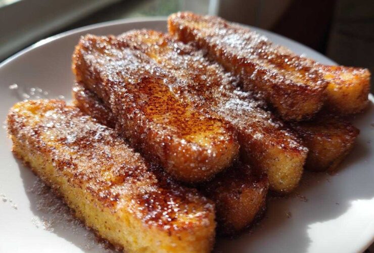 Close-up of golden Air Fryer French Toast Sticks coated heavily in sparkling cinnamon sugar on a white plate.