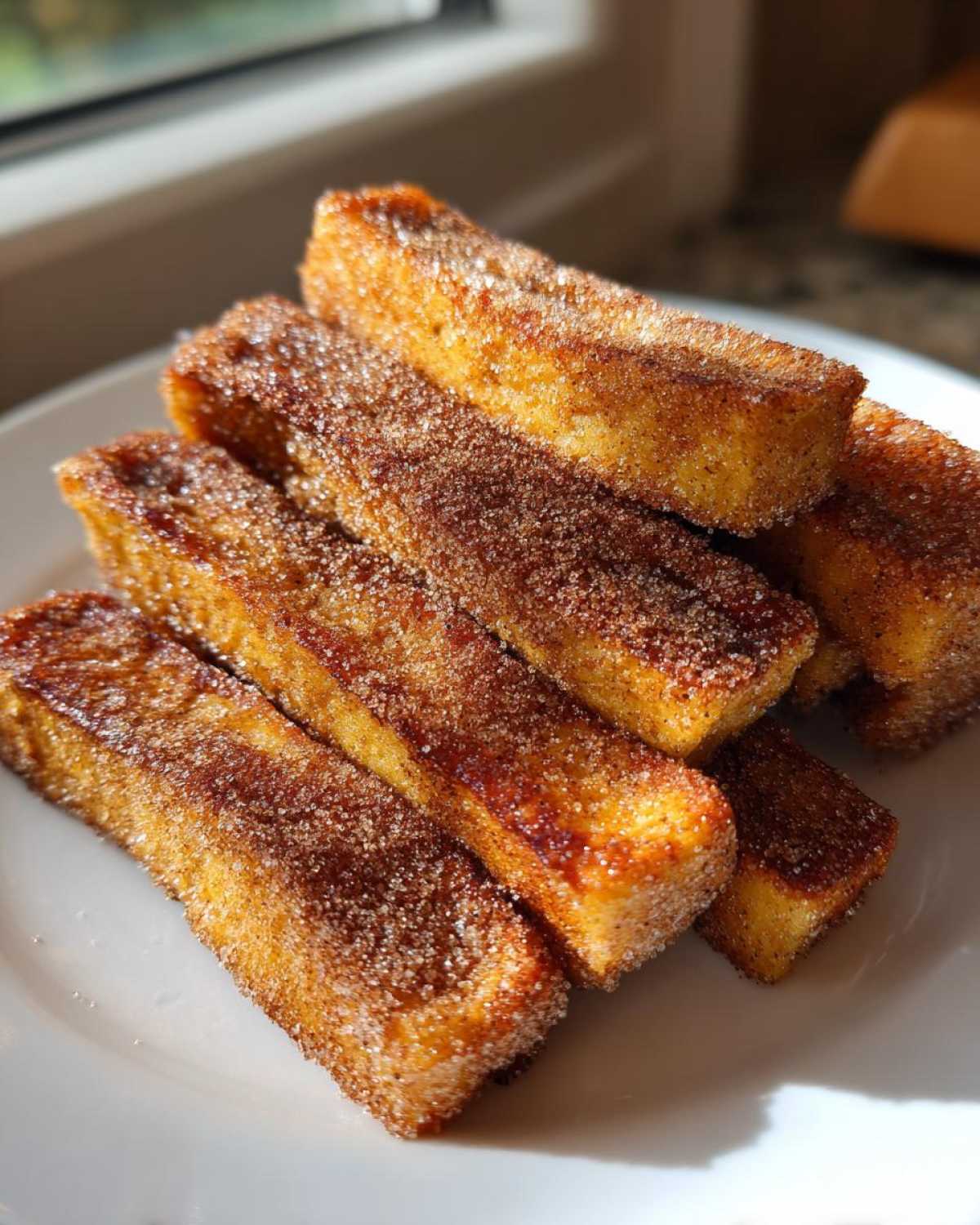 A stack of golden Air Fryer French Toast Sticks generously coated in sparkling cinnamon sugar on a white plate.