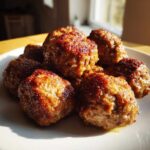 A close-up of several golden-brown, juicy Air Fryer Italian Meatballs piled on a white plate, catching the sunlight.