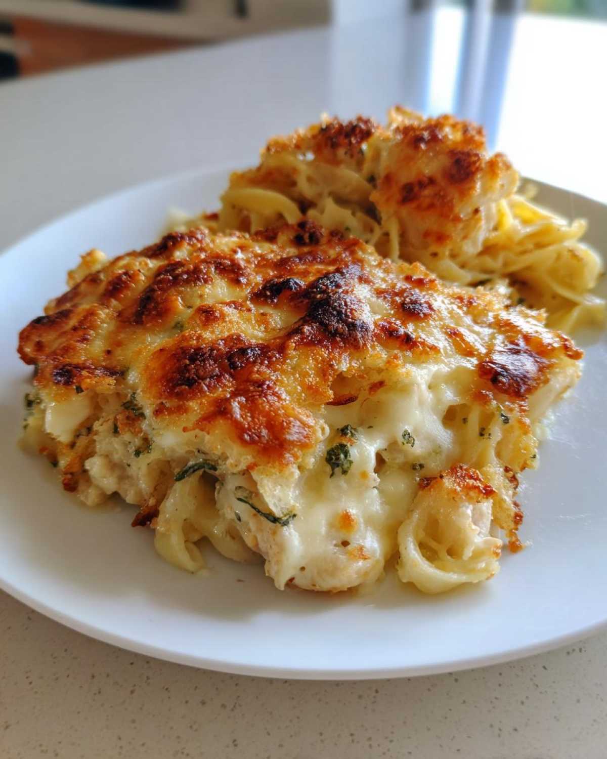A serving of Cheesy Baked Chicken Alfredo with Crispy Top showing creamy pasta and browned cheese crust.
