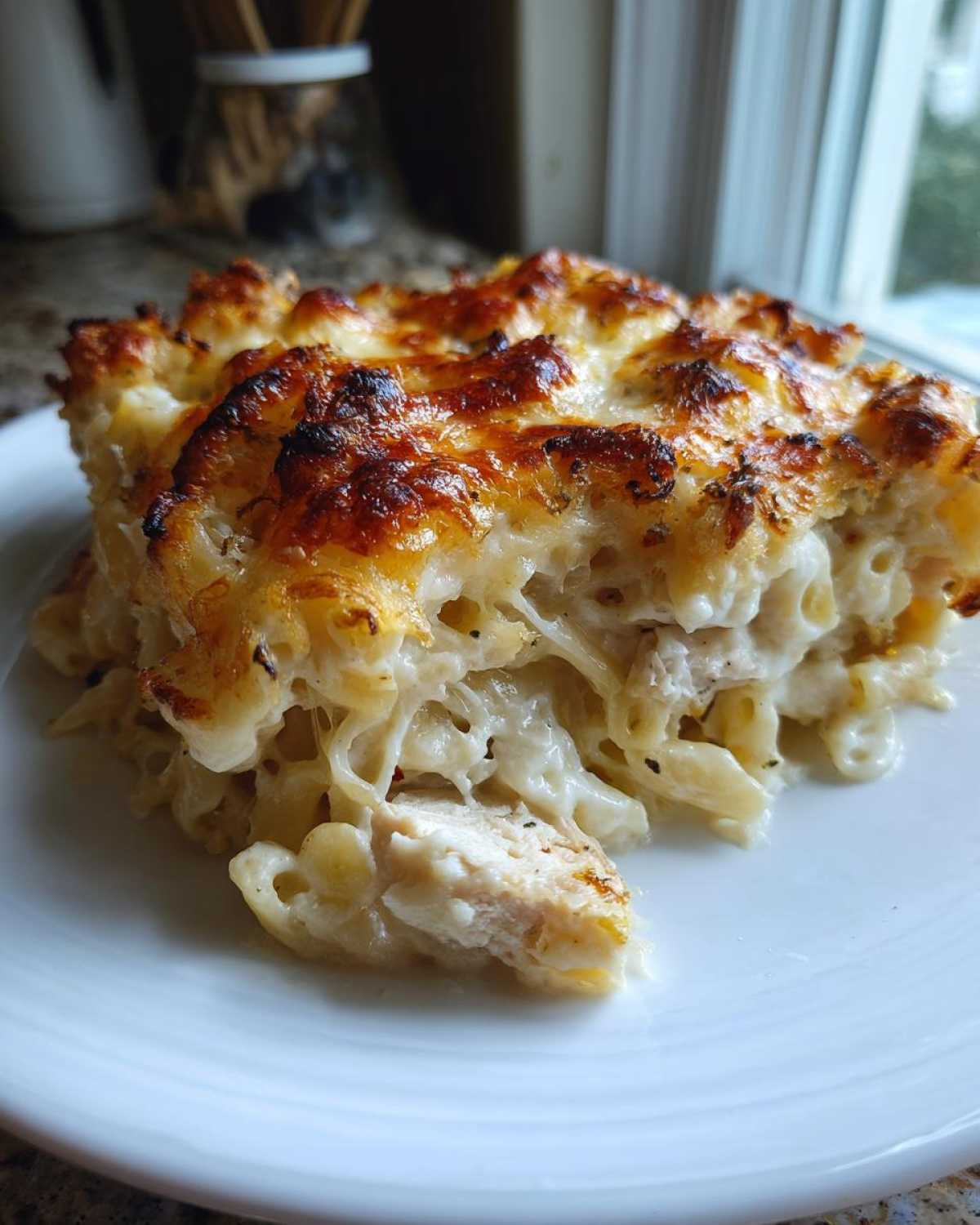 A close-up of a serving of Cheesy Chicken Alfredo Pasta Bake with Mozzarella, showing melted, browned cheese on top and creamy pasta with chicken pieces.