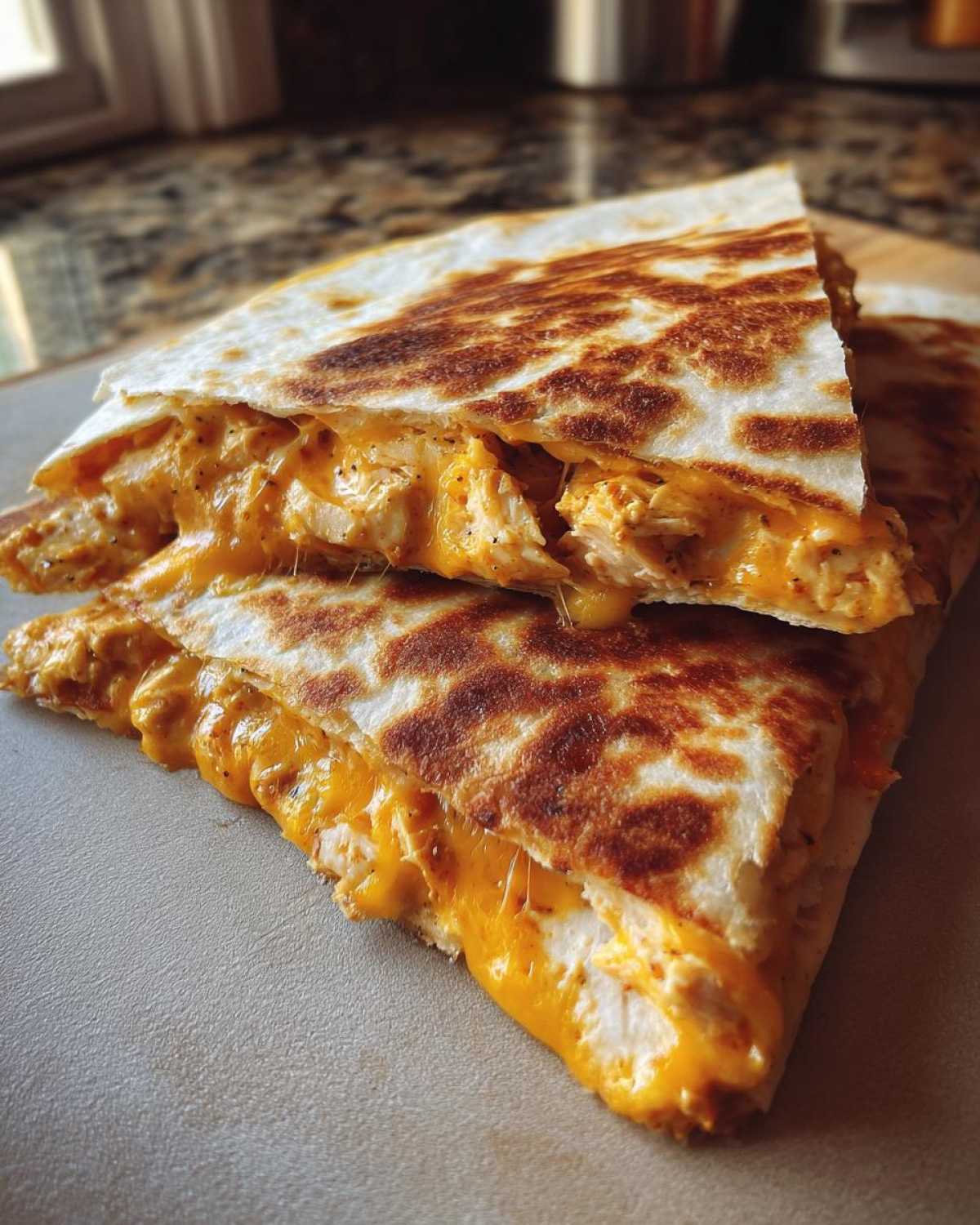 Close-up of a Cheesy Chicken Quesadilla cut in half, showing melted orange cheese oozing out with shredded chicken.
