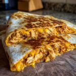 Close-up of a Cheesy Chicken Quesadilla with Crispy Tortilla cut in half, showing melted cheese and shredded chicken filling.