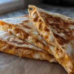 Four stacked wedges of Cheesy Chicken Quesadilla with crispy, golden-brown tortillas showing melted cheese and shredded chicken filling.