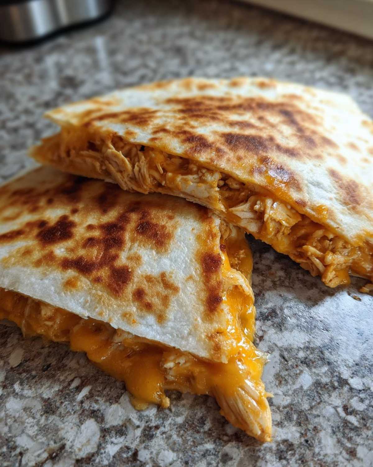 Two halves of a Cheesy Chicken Quesadilla showing melted orange cheese and shredded chicken filling inside a golden-brown tortilla.