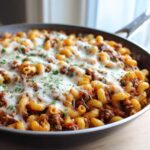 Close-up of a Cheesy Ground Beef Pasta Skillet topped with melted mozzarella and fresh parsley in a large pan.
