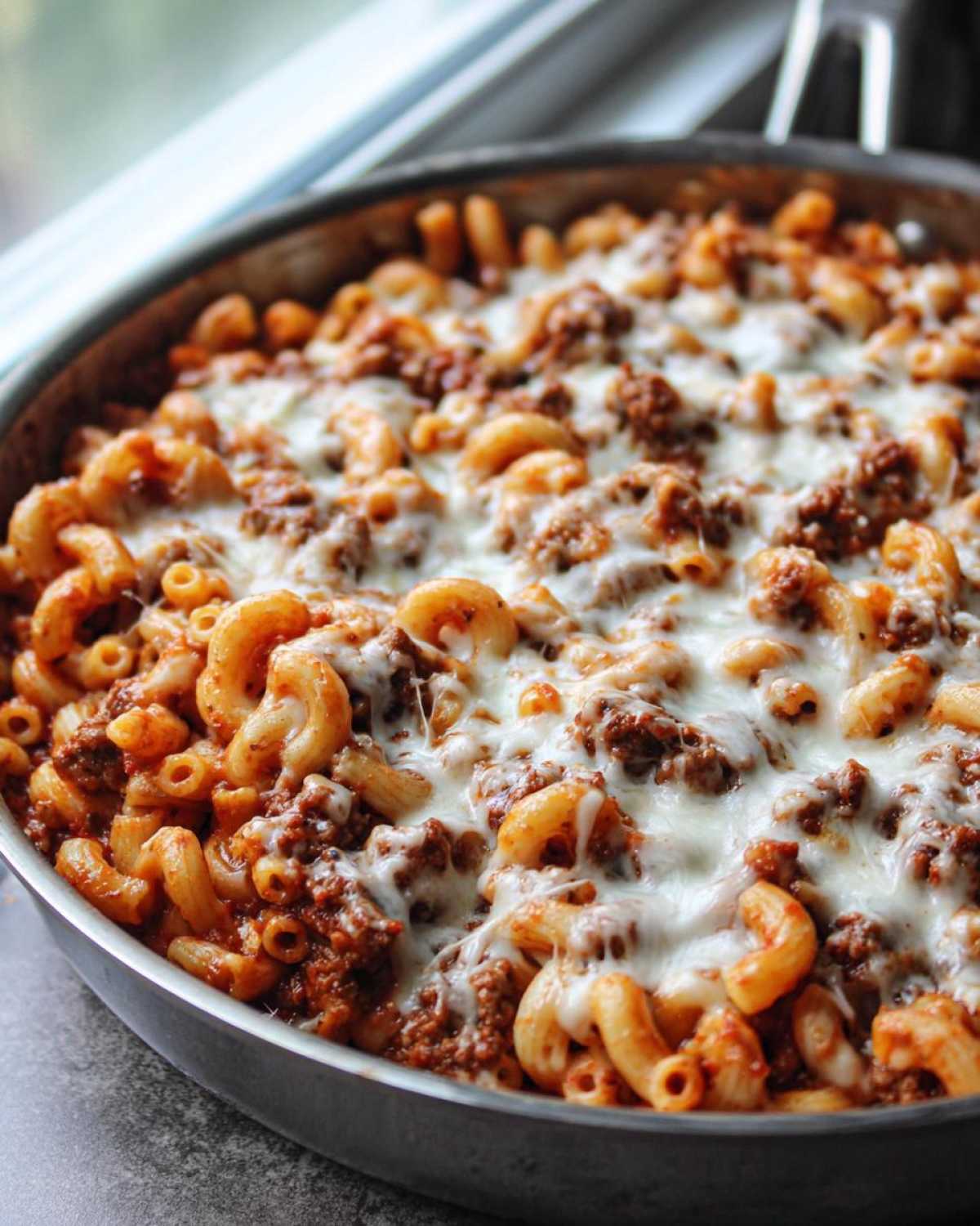 Close-up of a Cheesy Ground Beef Pasta Skillet topped with melted mozzarella cheese in a metal pan.