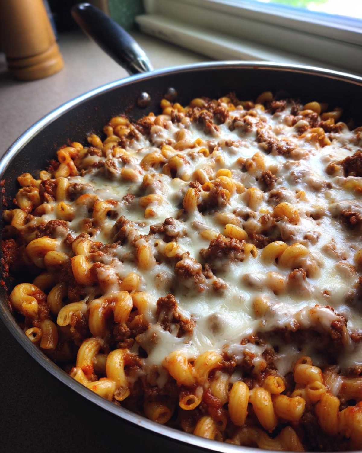 A close-up of a Cheesy Ground Beef Pasta Skillet topped with melted mozzarella cheese in a black skillet.
