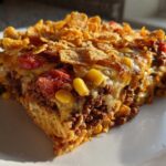 A hearty slice of Cheesy Ground Beef Queso Bake Comfort Dish topped with melted cheese, corn, tomatoes, and crunchy cornflakes.
