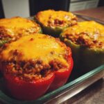 Four Cheesy Ground Beef Stuffed Peppers with Rice, topped with melted cheddar cheese, resting in a glass baking dish.