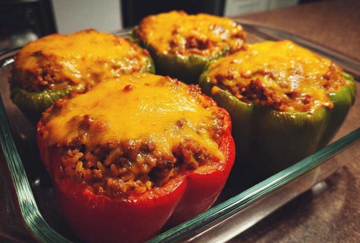 Four Cheesy Ground Beef Stuffed Peppers with Rice, topped with melted cheddar cheese, resting in a glass baking dish.