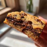 A close-up view of a thick, chewy chocolate chip cookie bars slice showing gooey, melted chocolate chips.