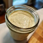 Close-up of creamy, pale green Copycat Olive Garden Salad Dressing stored in a glass mason jar.