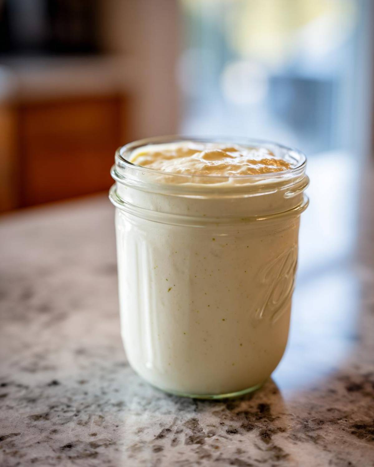 Creamy Copycat Olive Garden Salad Dressing stored in a clear glass mason jar on a granite countertop.