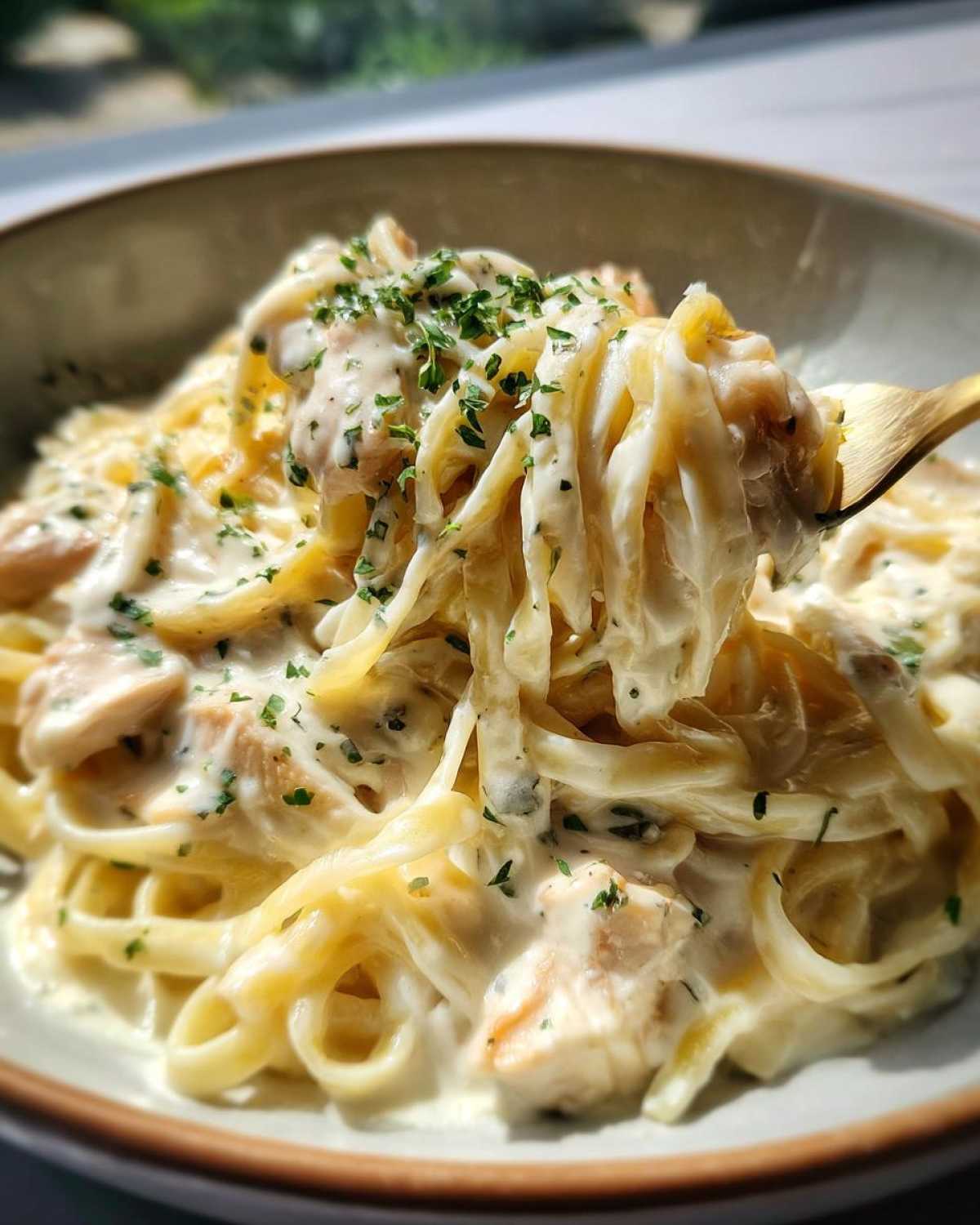 A close-up of a fork lifting fettuccine noodles coated in rich sauce from a bowl of Creamy Alfredo Chicken Pasta Easy Recipe.