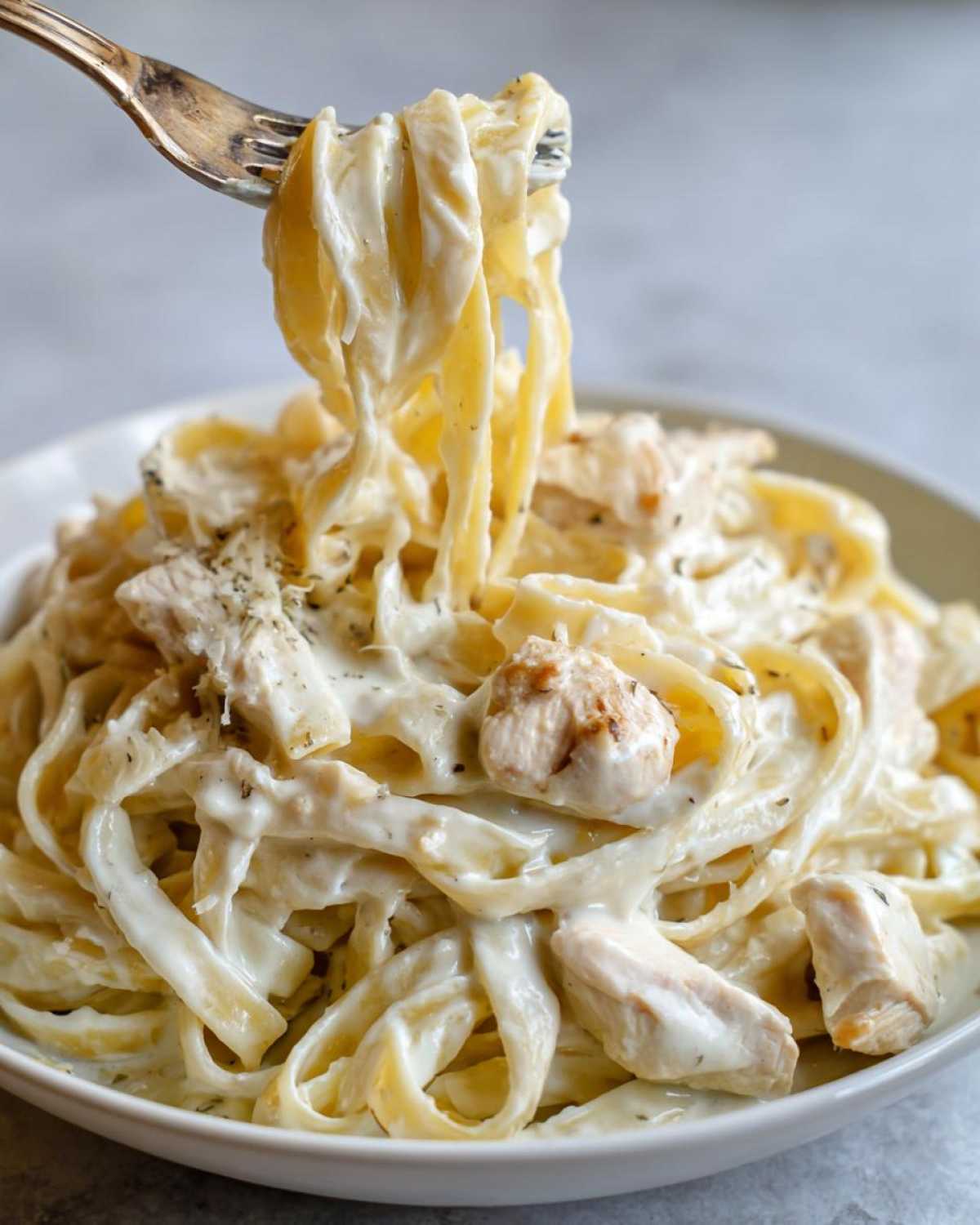 A fork lifting fettuccine noodles coated in rich sauce and chunks of chicken from a bowl of Creamy Alfredo Chicken Pasta Easy Recipe.
