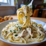 A fork lifting a large swirl of fettuccine noodles coated in rich sauce from a bowl of Creamy Alfredo Chicken Pasta Easy Recipe.
