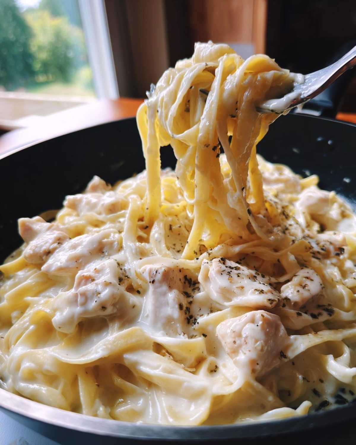 A fork lifting fettuccine noodles coated in rich sauce from a pan of Creamy Alfredo Chicken Pasta Easy Recipe.