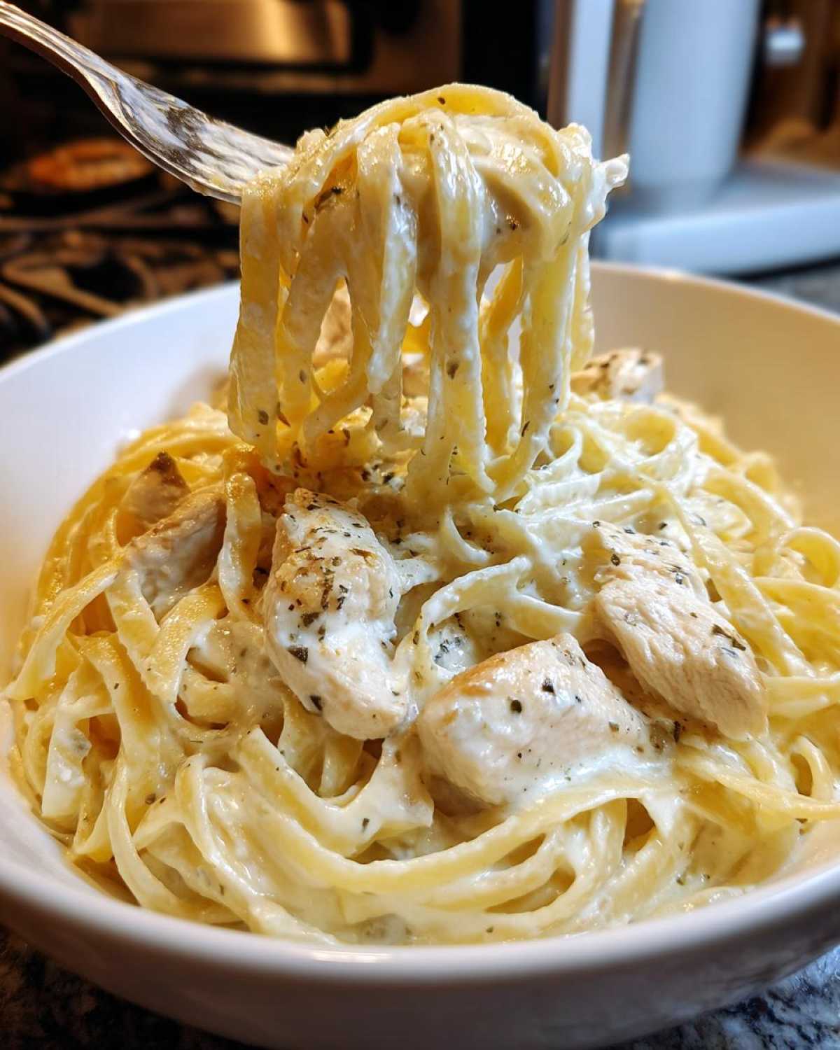A fork lifting fettuccine noodles coated in rich sauce from a bowl of Creamy Alfredo Chicken Pasta Easy Recipe.
