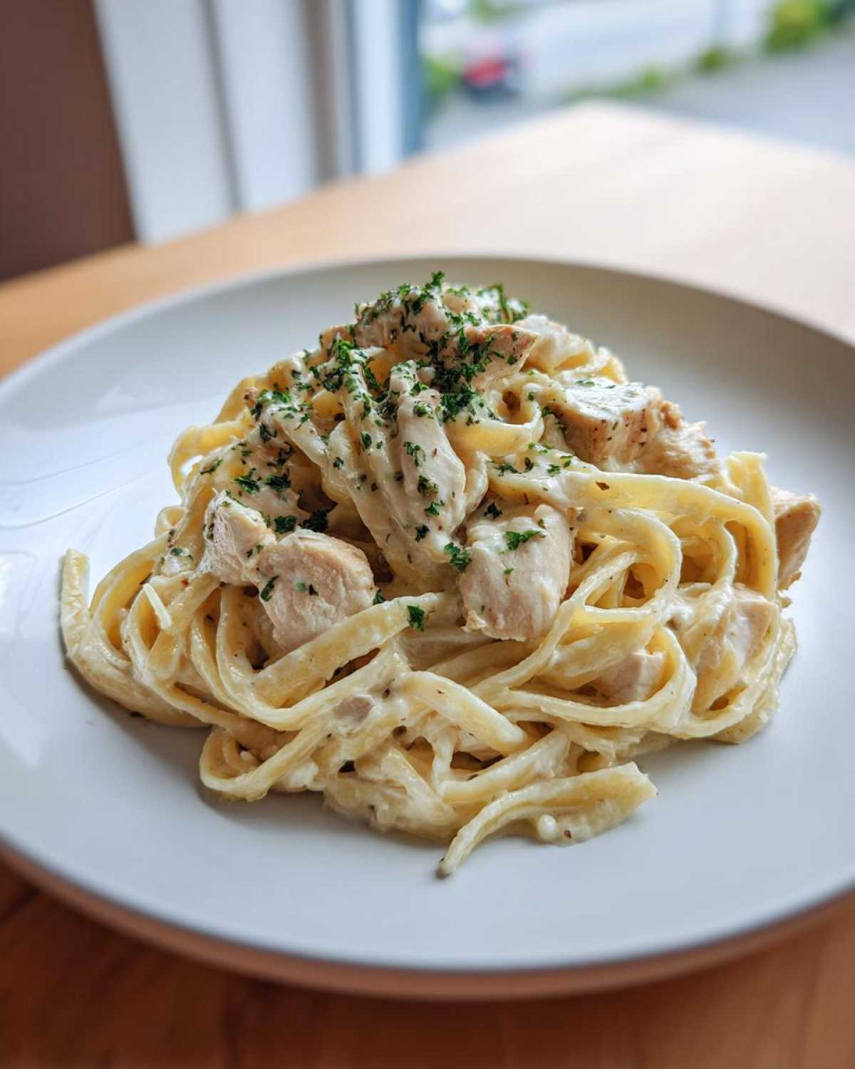 A close-up of fettuccine pasta coated in rich sauce with chunks of chicken, garnished with parsley, representing Creamy Alfredo Pasta with Chicken and Cheese.