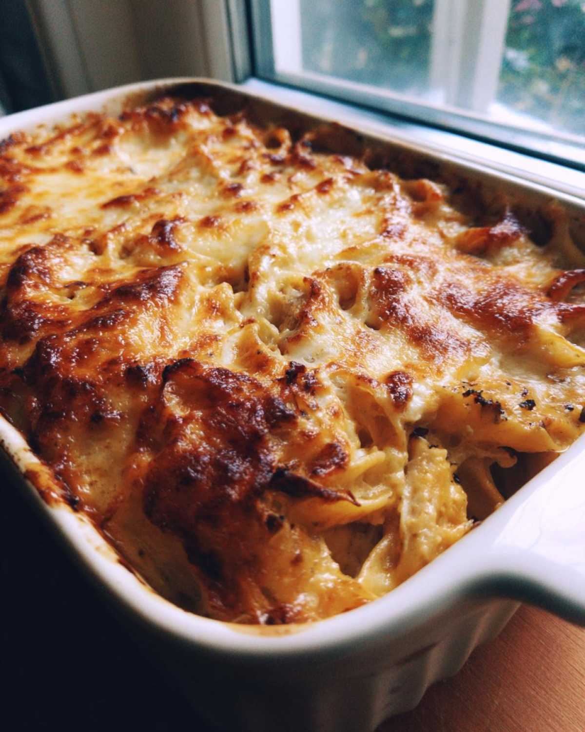 Close-up of a Creamy Cajun Chicken Alfredo Bake with a golden, bubbly, and slightly browned cheese topping in a white baking dish.