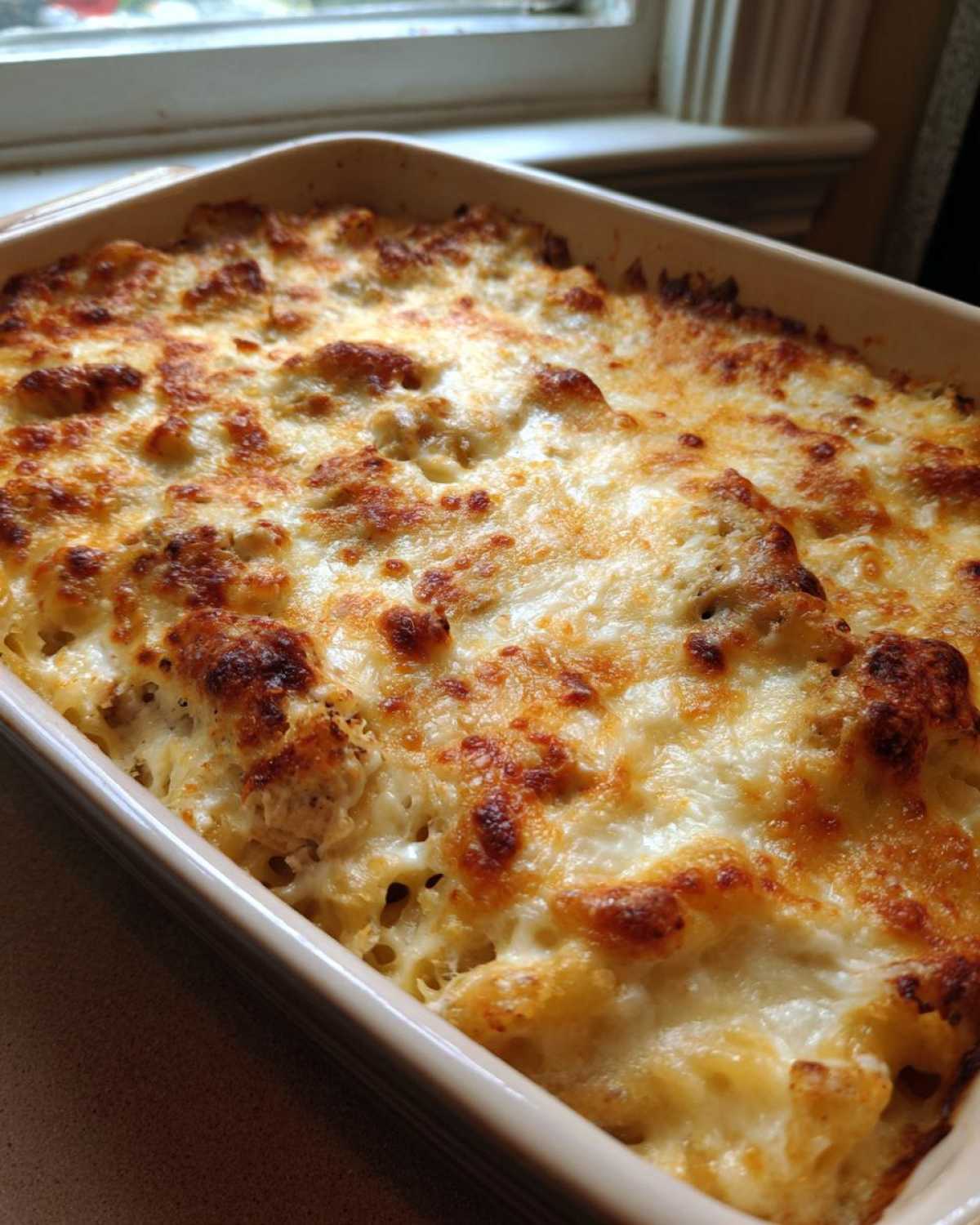 Close-up of a baked casserole dish topped with bubbly, browned cheese, featuring the Creamy Cajun Chicken Alfredo Bake.