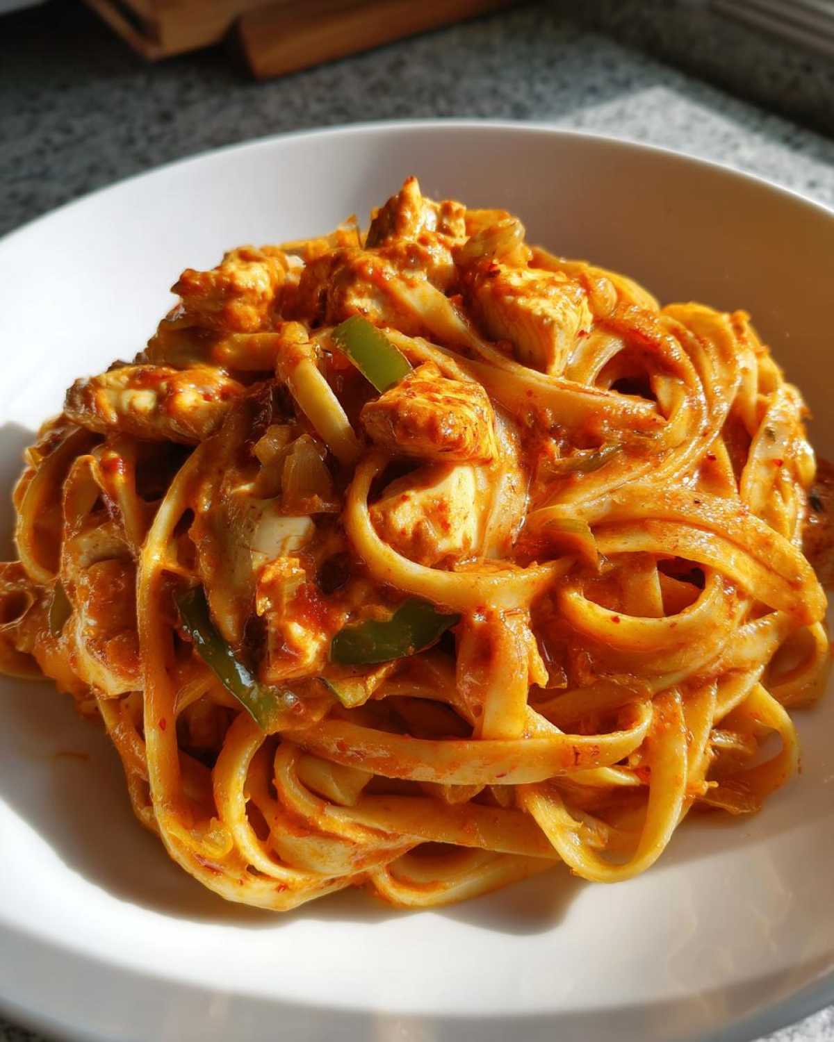 A close-up of Creamy Cajun Chicken Pasta with bold flavor, featuring fettuccine coated in a rich orange sauce with chicken chunks and green peppers.