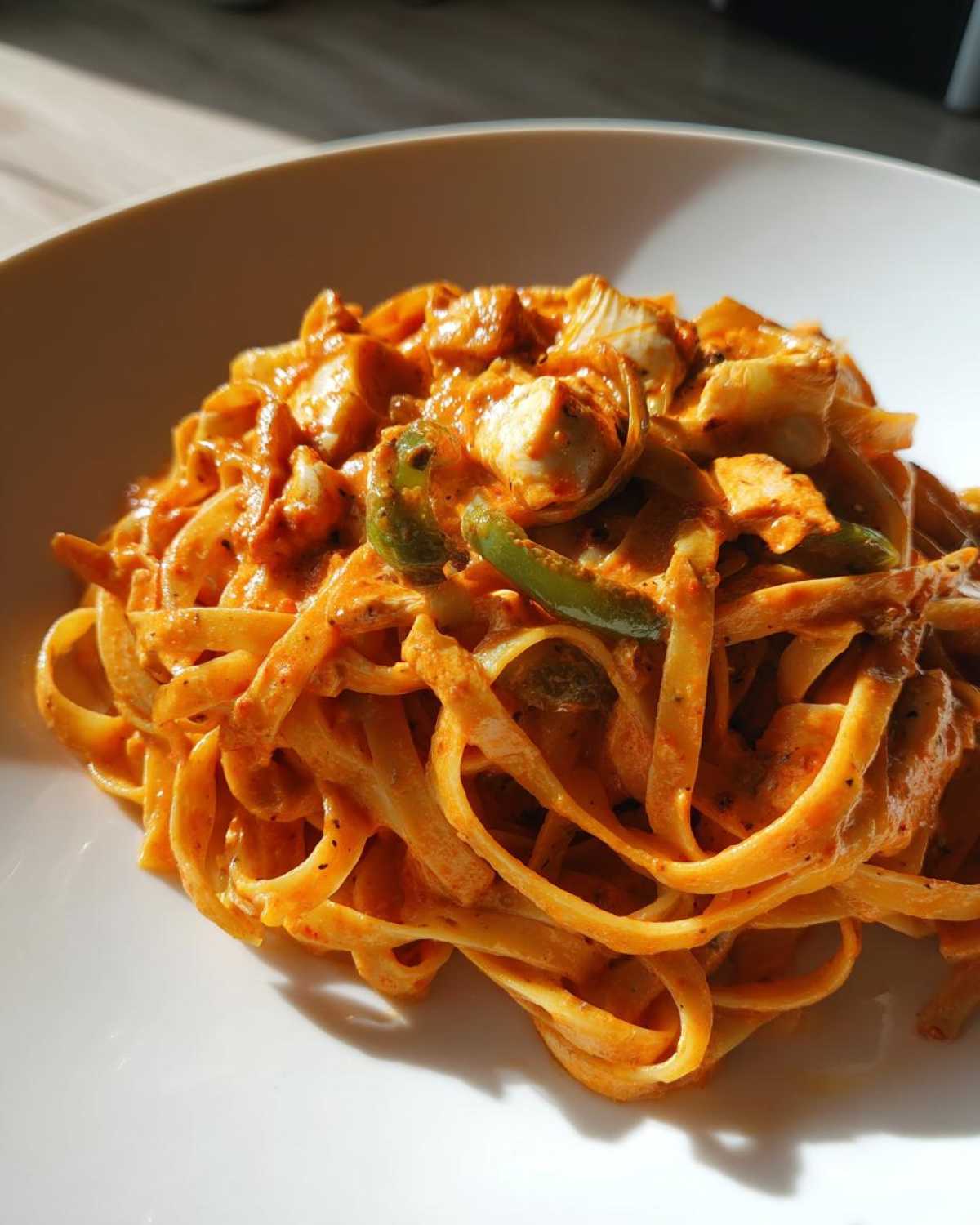 Close-up of a bowl of Creamy Cajun Chicken Pasta with fettuccine, chicken, and green peppers in a rich sauce.