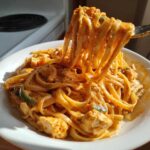 A fork lifting fettuccine noodles coated in orange sauce from a bowl of Creamy Cajun Chicken Pasta with chicken chunks and green peppers.