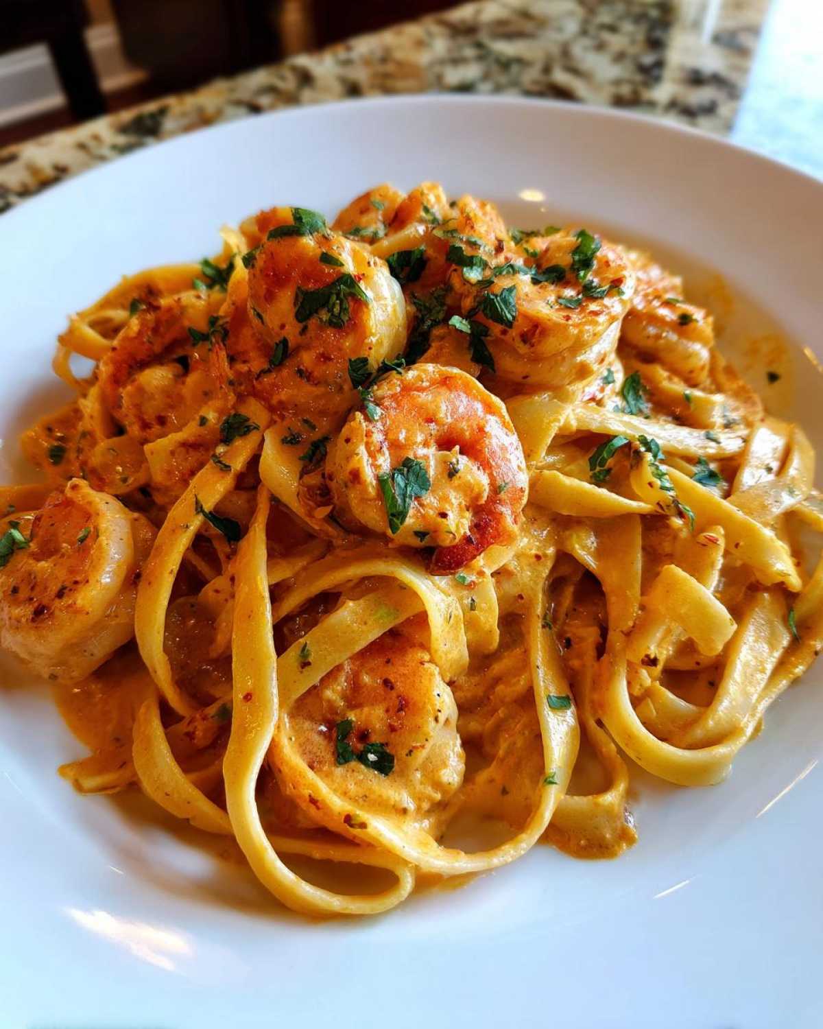 Close-up of Creamy Cajun Shrimp Pasta featuring large shrimp coated in a rich, orange sauce over fettuccine, garnished with parsley.