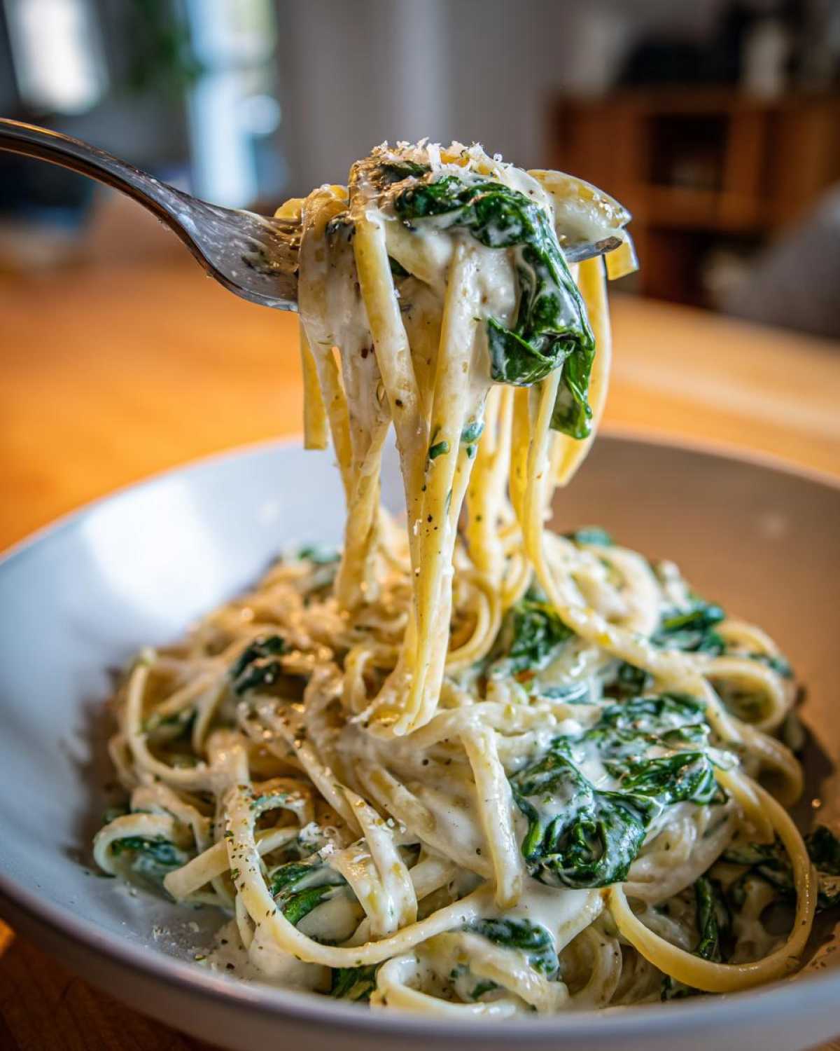 A fork lifting a generous twirl of Creamy Lemon Ricotta Pasta with Spinach coated in a rich white sauce.