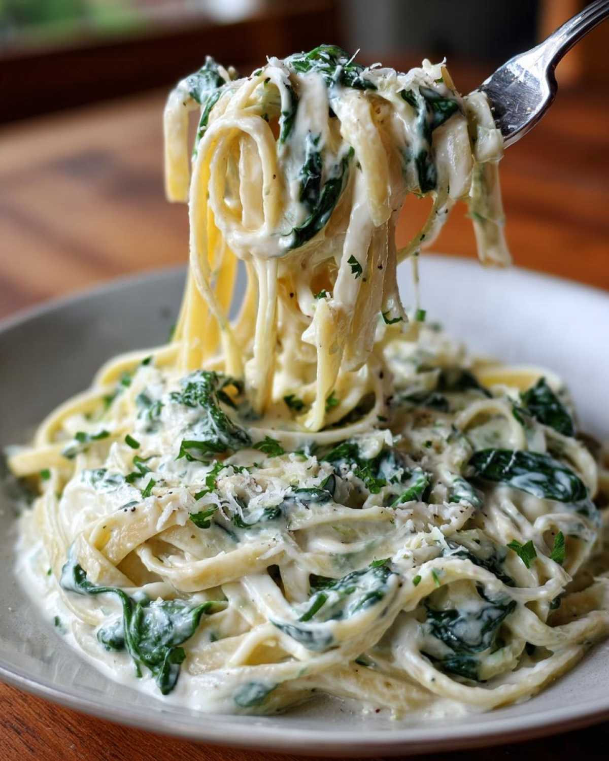 A fork lifts a twirl of fettuccine coated in creamy sauce, spinach, and cheese from a bowl of Creamy Lemon Ricotta Pasta with Spinach.