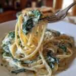 A fork lifts a bite of linguine coated in creamy sauce and spinach from a plate of Creamy Lemon Ricotta Pasta with Spinach.